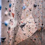 Wide angle view of Caucasian athlete in late 20s practicing on vertical wall in modern indoor rock climbing gym.